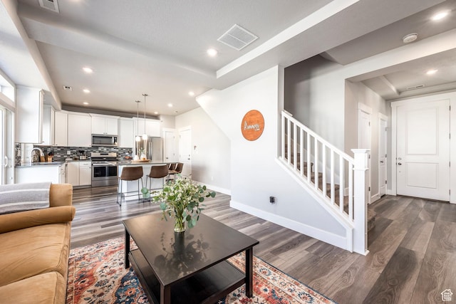 living room featuring dark wood-style flooring, visible vents, stairway, and baseboards