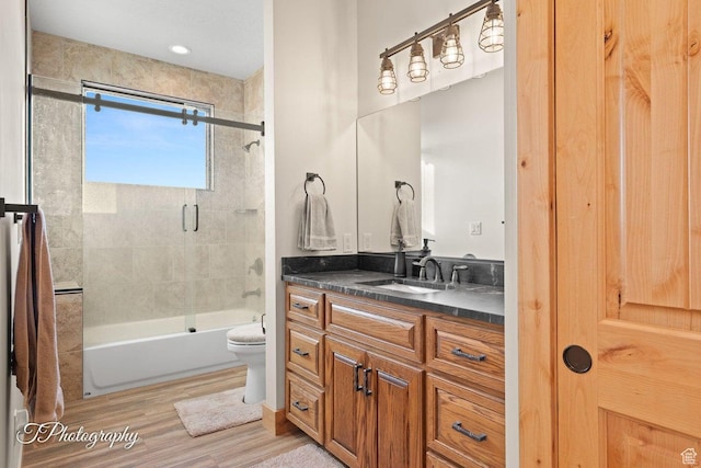 full bathroom with hardwood / wood-style floors, shower / bath combination with glass door, vanity, and toilet