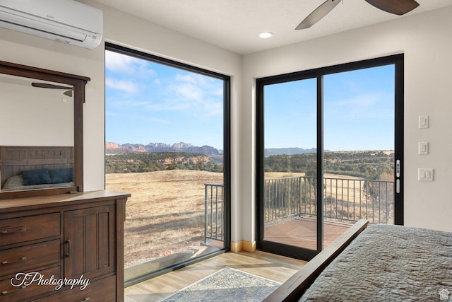 bedroom with ceiling fan, light hardwood / wood-style floors, a mountain view, a wall unit AC, and access to exterior