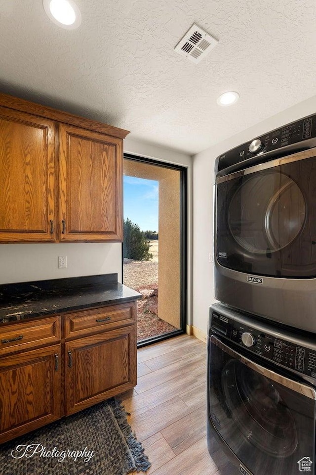 laundry room with cabinets, a textured ceiling, stacked washer and clothes dryer, and light wood-type flooring