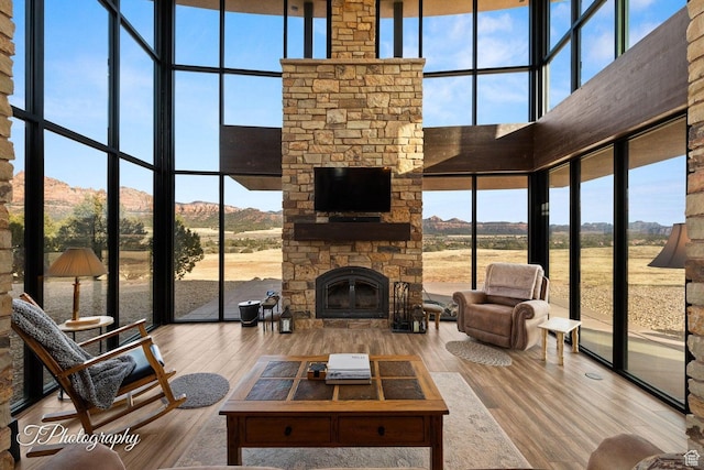 living room featuring a healthy amount of sunlight, hardwood / wood-style flooring, a towering ceiling, and a stone fireplace