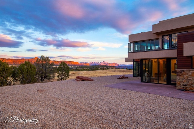 yard at dusk with a mountain view, a balcony, and a patio