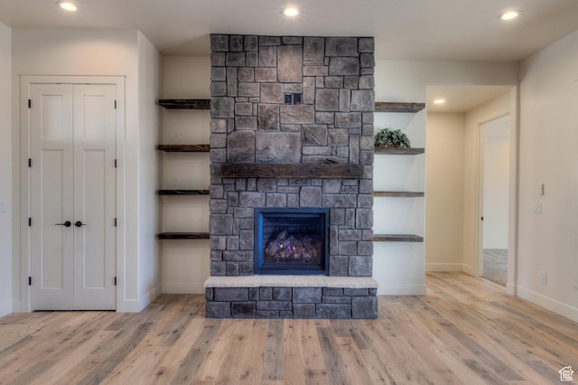 unfurnished living room with built in shelves, a stone fireplace, and light hardwood / wood-style flooring