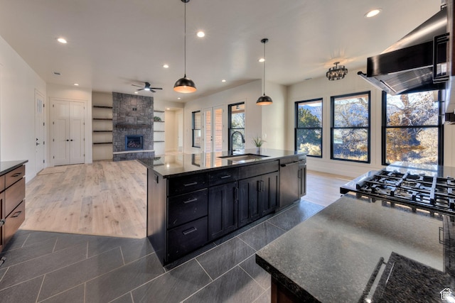 kitchen featuring pendant lighting, sink, extractor fan, dark stone countertops, and a center island with sink