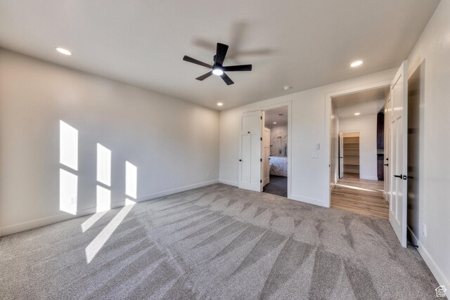 unfurnished bedroom with ceiling fan, a closet, a spacious closet, and light carpet