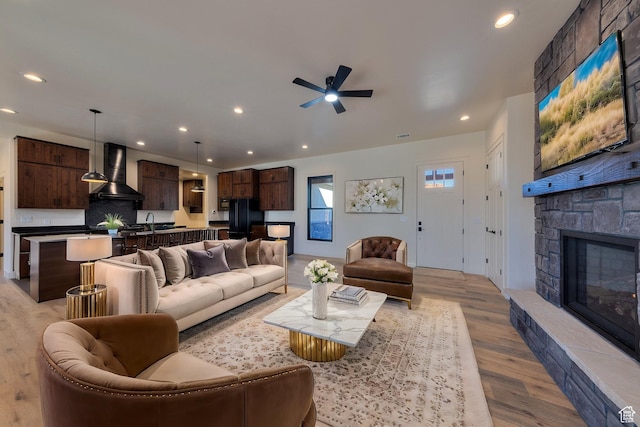 living room with ceiling fan, a stone fireplace, and light wood-type flooring