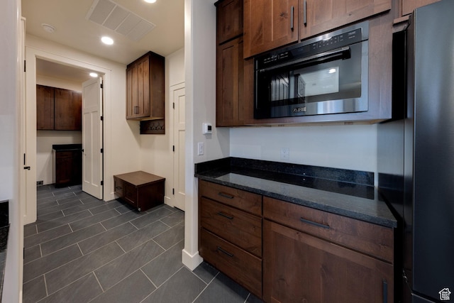 kitchen featuring black refrigerator, dark tile patterned flooring, and dark stone counters