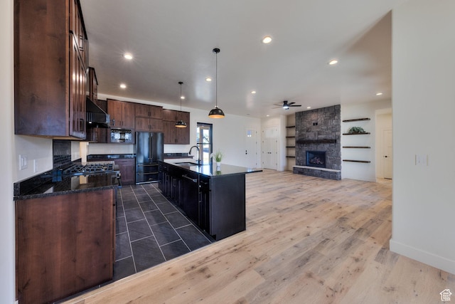 kitchen featuring high end black refrigerator, sink, decorative light fixtures, wall chimney exhaust hood, and an island with sink