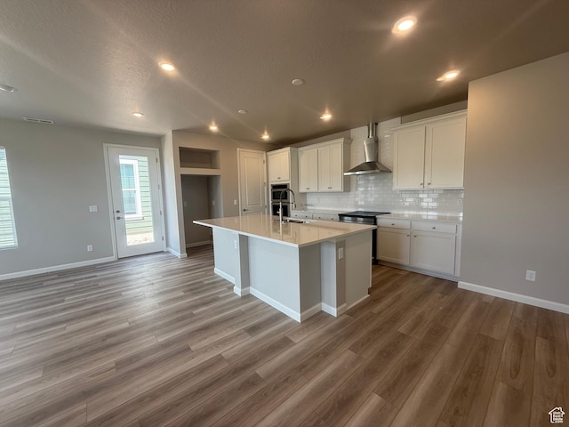 6158 W 11800 S Unit 504, South Jordan, UT 84009 - kitchen featuring wall chimney exhaust hood, white cabinets, decorative backsplash, light wood finished floors, and a center island with sink
