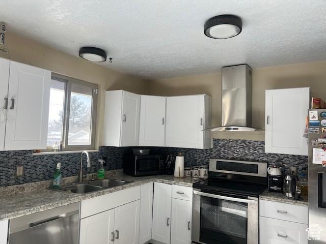 kitchen with appliances with stainless steel finishes, a textured ceiling, white cabinetry, sink, and wall chimney exhaust hood