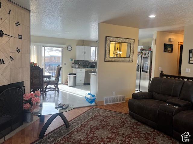 living room featuring a tile fireplace, a textured ceiling, and light hardwood / wood-style flooring
