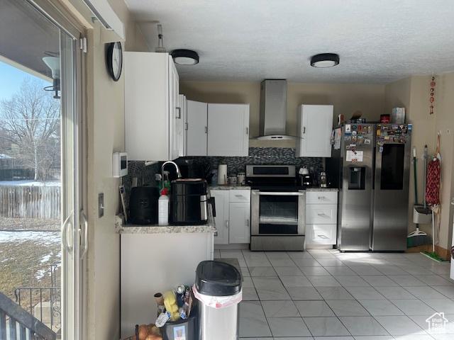 kitchen with appliances with stainless steel finishes, wall chimney exhaust hood, white cabinetry, light tile patterned flooring, and decorative backsplash