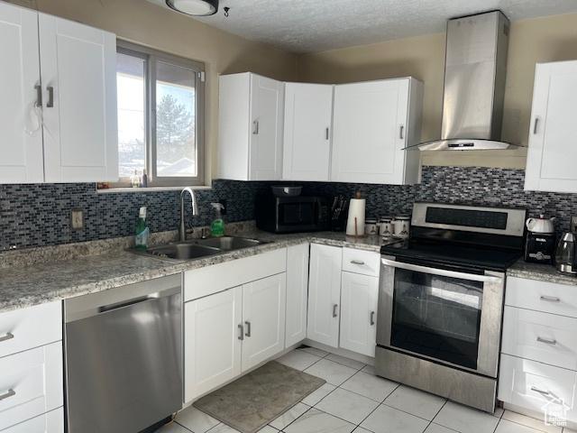 kitchen featuring wall chimney range hood, white cabinets, appliances with stainless steel finishes, and sink