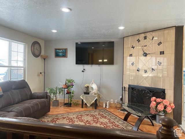 living room with hardwood / wood-style floors, a textured ceiling, and a tiled fireplace