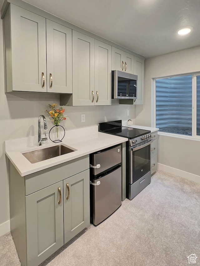 kitchen featuring stainless steel appliances, gray cabinets, light countertops, and a sink