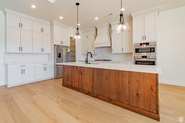 kitchen with a center island with sink, pendant lighting, white cabinetry, and custom range hood