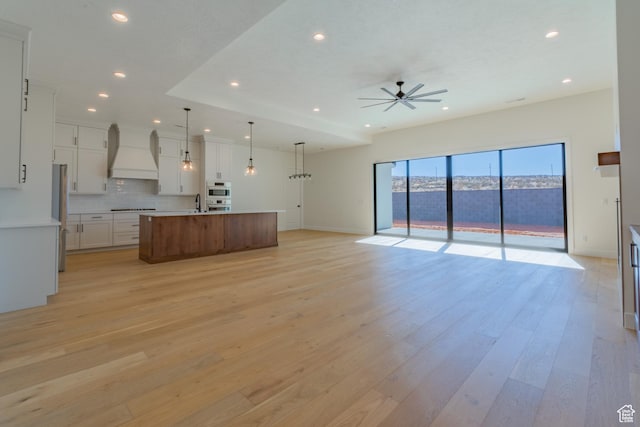kitchen featuring hanging light fixtures, a large island, premium range hood, white cabinetry, and stainless steel refrigerator