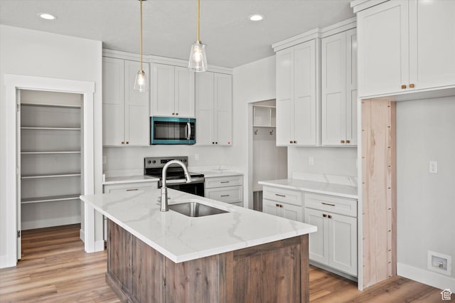 kitchen with light stone countertops, light wood-style floors, appliances with stainless steel finishes, baseboards, and a center island with sink