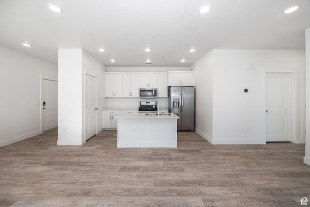 kitchen with white cabinets, appliances with stainless steel finishes, light hardwood / wood-style flooring, and an island with sink