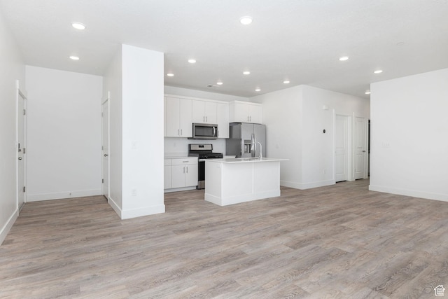 kitchen with a center island with sink, light wood-type flooring, white cabinets, and appliances with stainless steel finishes