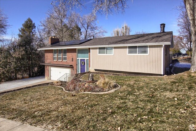 bi-level home featuring a garage, solar panels, and a front yard
