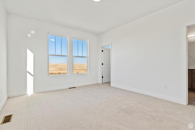 spare room featuring light carpet and baseboards