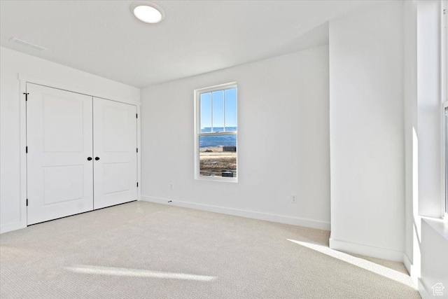 unfurnished bedroom featuring light carpet, baseboards, and a closet