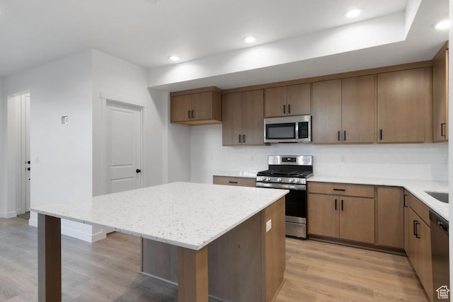 7091 W S Jordan Pkwy Unit 394, South Jordan, UT 84009 - kitchen featuring appliances with stainless steel finishes, backsplash, light wood-type flooring, a kitchen island, and light stone countertops