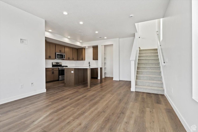 kitchen with stainless steel appliances, open floor plan, baseboards, wood finished floors, and light countertops