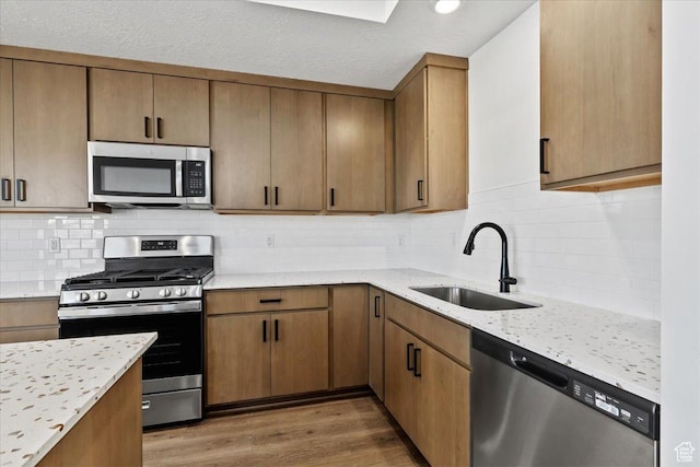 kitchen with stainless steel appliances, a sink, wood finished floors, decorative backsplash, and light stone counters