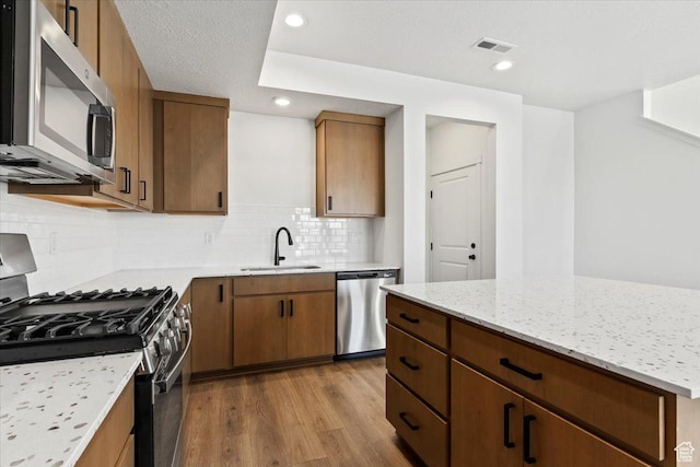 kitchen featuring appliances with stainless steel finishes, a sink, dark wood-style floors, decorative backsplash, and light stone countertops