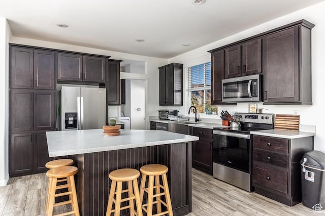 kitchen featuring a kitchen island, stainless steel appliances, sink, a breakfast bar, and light hardwood / wood-style flooring