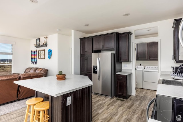 kitchen with a center island, dark brown cabinetry, washing machine and dryer, a breakfast bar area, and stainless steel fridge