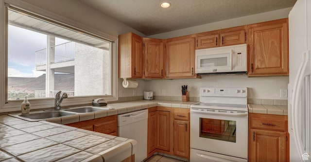 kitchen with sink, light tile patterned flooring, white appliances, tile countertops, and a textured ceiling