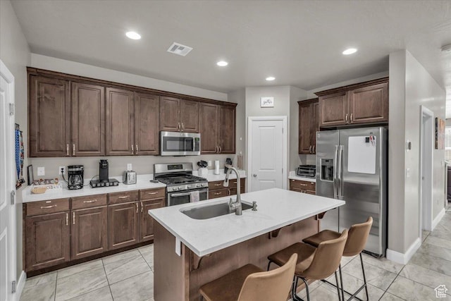 kitchen with sink, stainless steel appliances, an island with sink, a breakfast bar area, and dark brown cabinetry