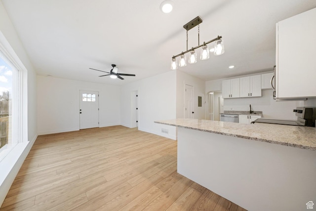 kitchen with appliances with stainless steel finishes, pendant lighting, white cabinets, light stone counters, and light hardwood / wood-style flooring