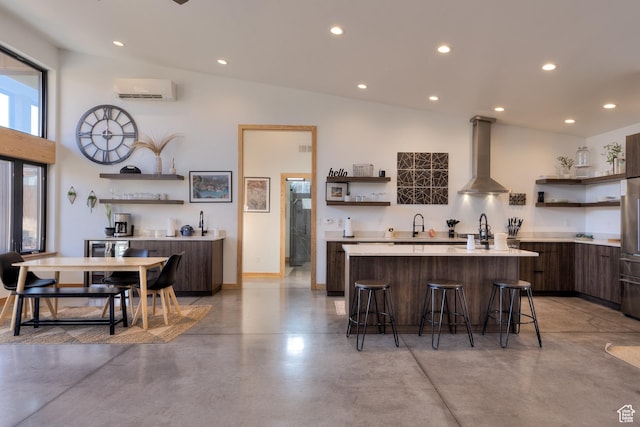 171 E Mt Peale Dr, Moab, UT 84532 - kitchen featuring a center island, wall chimney range hood, dark brown cabinets, a wall mounted AC, and a breakfast bar area
