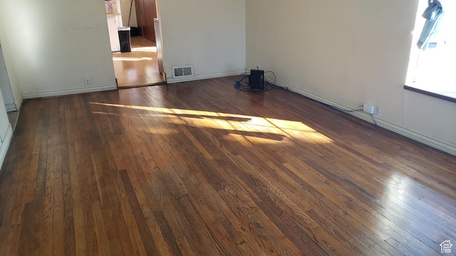 spare room featuring baseboards, dark wood-type flooring, and visible vents