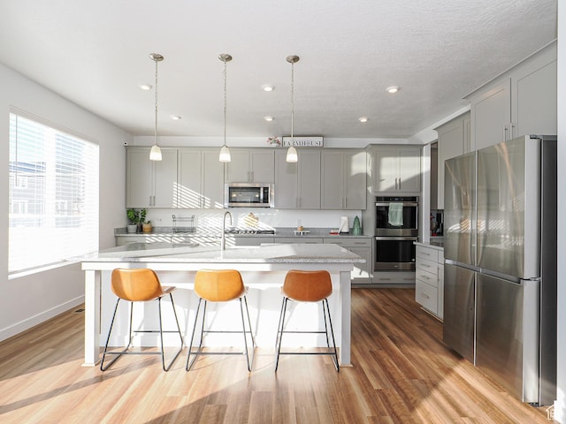 1766 E Johnstown Rd N Unit 710, Eagle Mountain, UT 84005 - kitchen featuring appliances with stainless steel finishes, a breakfast bar, light wood finished floors, gray cabinets, and a center island with sink
