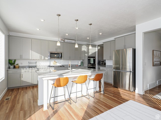 1766 E Johnstown Rd N Unit 710, Eagle Mountain, UT 84005 - kitchen with appliances with stainless steel finishes, a kitchen breakfast bar, an island with sink, light wood-style flooring, and gray cabinetry