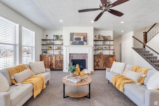 carpeted living room featuring ceiling fan, a brick fireplace, and a textured ceiling