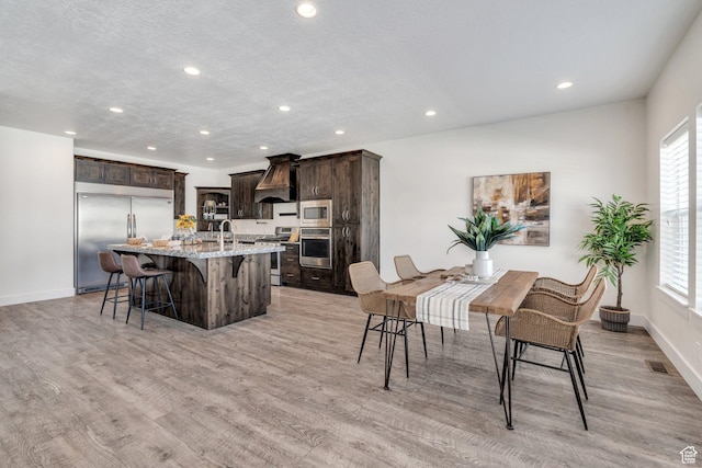 kitchen featuring a kitchen bar, light stone counters, built in appliances, an island with sink, and custom range hood
