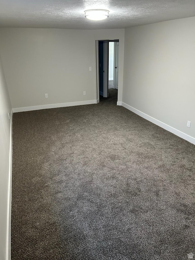 spare room featuring dark carpet and a textured ceiling