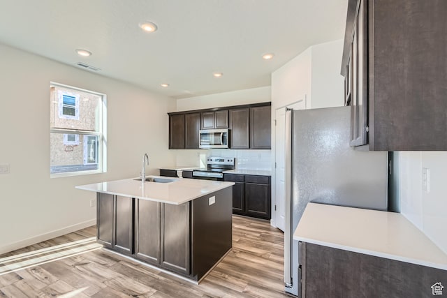kitchen with sink, an island with sink, light hardwood / wood-style flooring, and appliances with stainless steel finishes