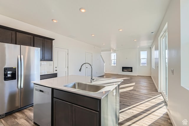 kitchen featuring a kitchen island with sink, sink, dark brown cabinets, light hardwood / wood-style flooring, and stainless steel appliances