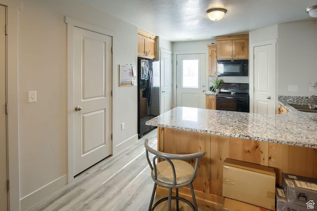 2460 W 450 N # 10, Tremonton, UT 84337 - kitchen featuring kitchen peninsula, sink, a kitchen breakfast bar, black appliances, and light stone countertops
