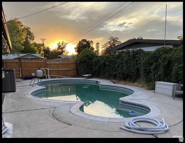 pool at dusk featuring cooling unit, a diving board, and a patio