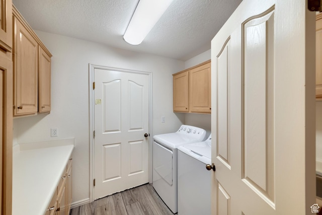 washroom featuring cabinet space, washing machine and clothes dryer, light wood-style flooring, and a textured ceiling