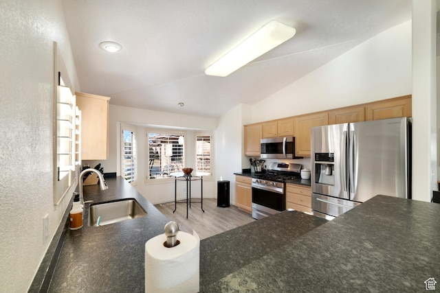 kitchen featuring appliances with stainless steel finishes, a sink, dark countertops, lofted ceiling, and light brown cabinets
