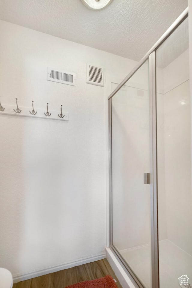 full bath featuring wood finished floors, a shower stall, a textured ceiling, and toilet
